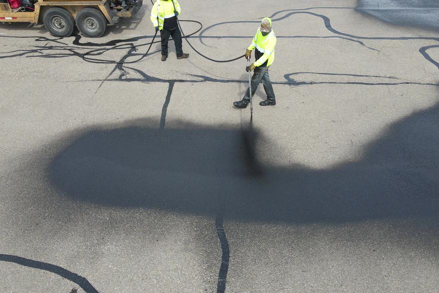 Crew applying sealcoat across an asphalt parking lot